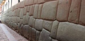 Side view of the Twelve Angled Stone Inca wall on Hatun Rumiyoq Street in Cusco, Peru, with large carved blocks and narrow sidewalk.