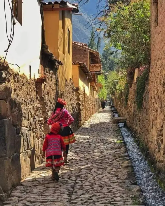 Una joven y su hija caminando por un sendero de piedras, con ropa tradicional y en día soleado.