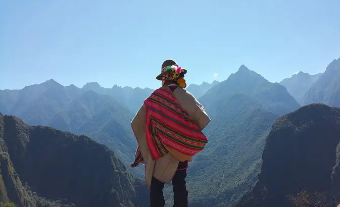A man standing on a high Andean viewpoint near Choquequirao, Cusco region, Peru, wearing a red poncho and looking over deep valleys.