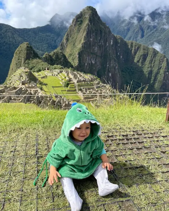 Baby smiling at Machu Picchu while wearing a crocodile-shaped coat