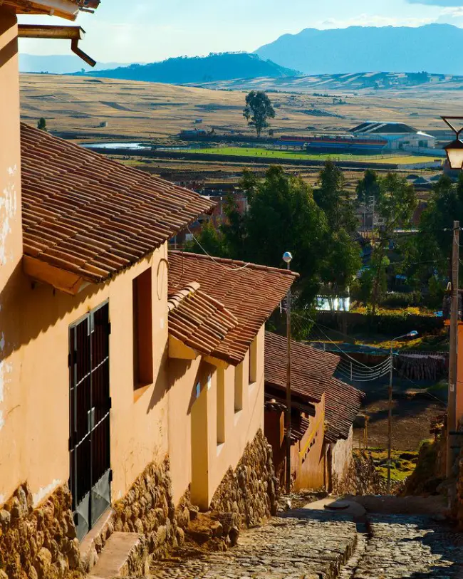 visit Chinchero Cusco rooftops houses steep lane valley view blue sky stones chinchero village