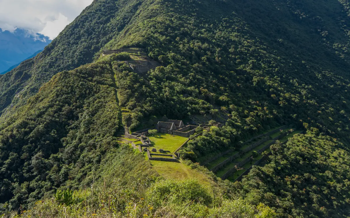 Choquequirao archaeological site seen from above, surrounded by green Andean mountains and agricultural terraces.