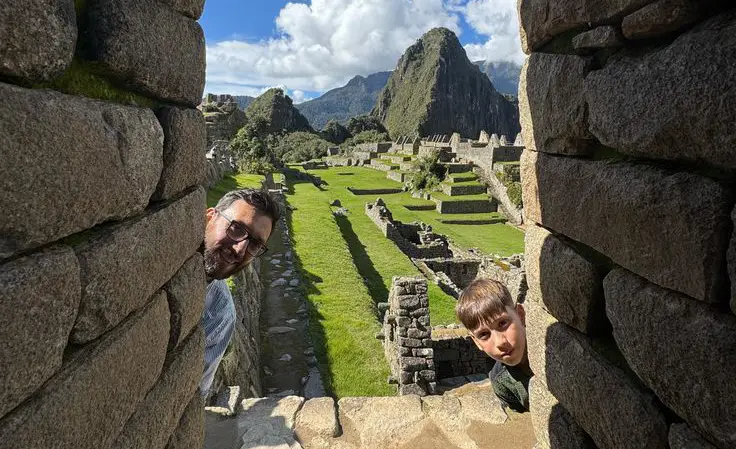 Father and son smiling under a stone arch during a family visit to Machu Picchu