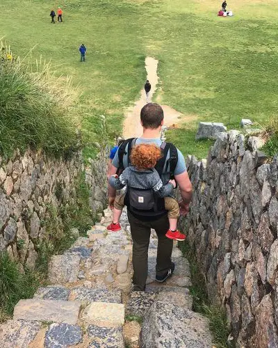 Father carrying his son in a baby carrier while descending stone stairs at Machu Picchu