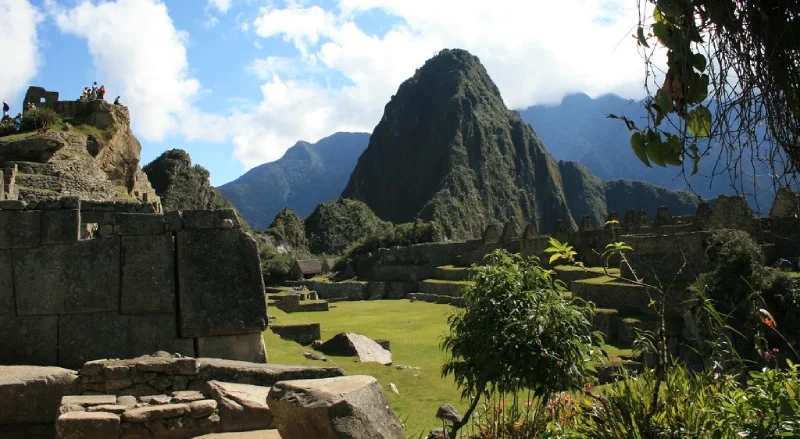 Ruinas y terrazas de piedra de Machu Picchu con la montaña Huayna Picchu al fondo, cielo brillante con nubes, Cusco, Perú destino icónico.