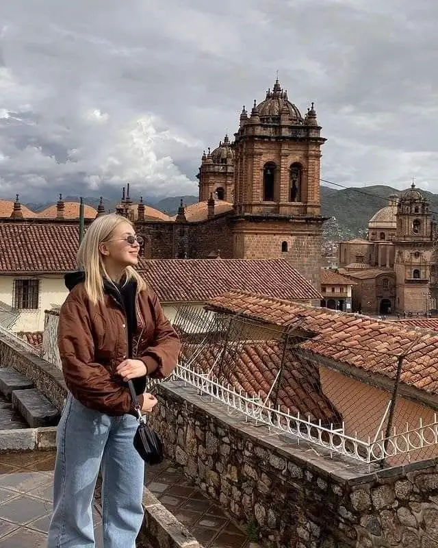 Muchacha sonriendo con la catedral principal de Cusco de fondo.