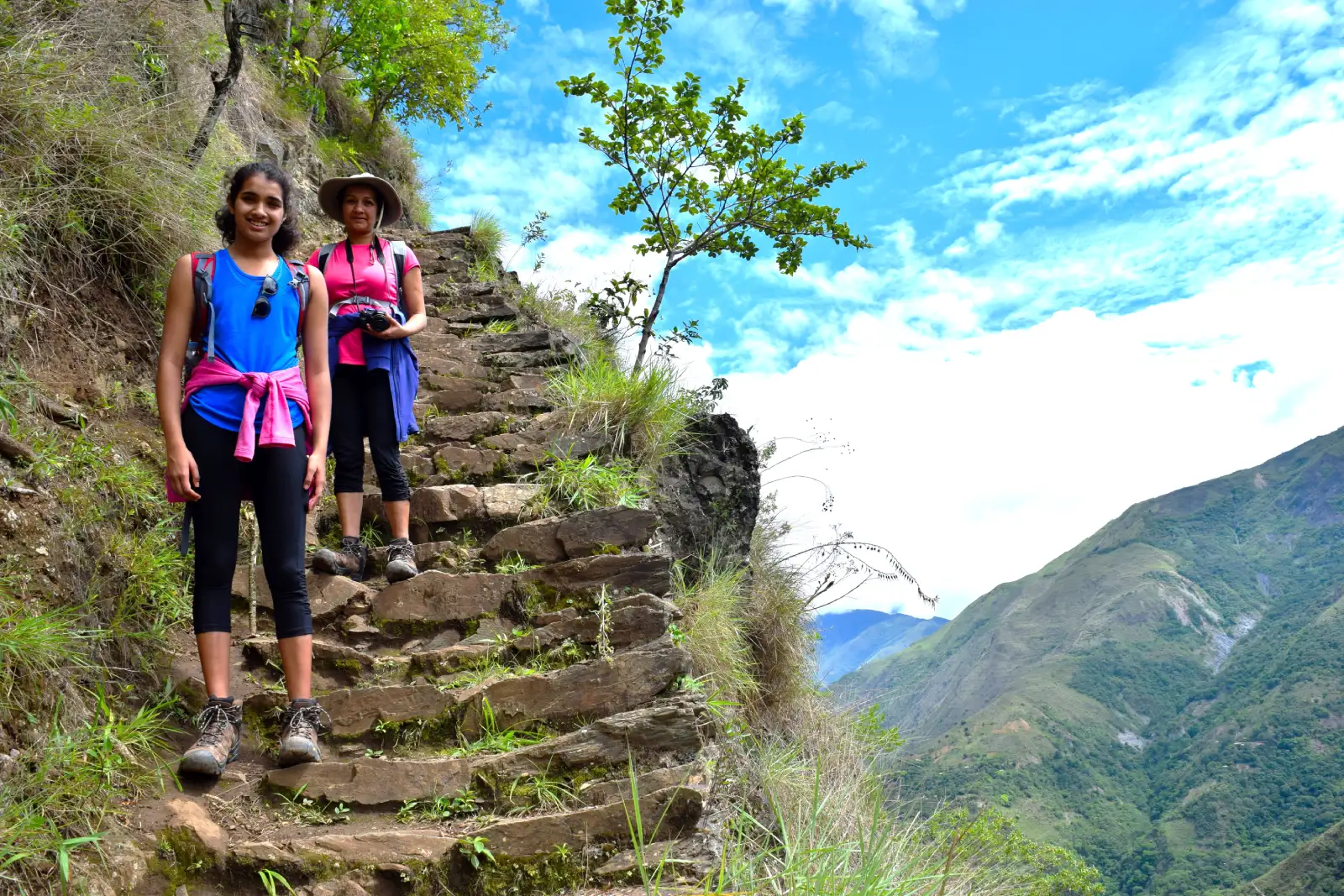 Travelers hiking on a stone trail during the Inca Jungle Trek, with green Andean valleys and mountain views.