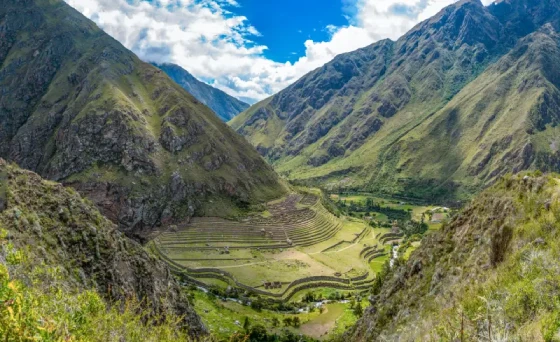 Wide Andean valley framed by dramatic mountains along the Inca Trail to Machu Picchu, with soft clouds and lush slopes near Cusco.