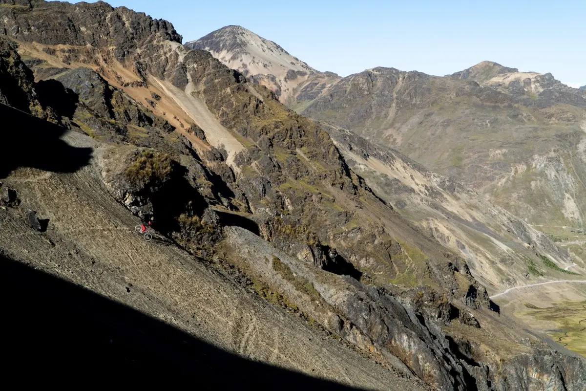 Cyclist riding the high Andean Lares route in Cusco, among steep mountains, rocky terrain, and remote valleys illuminated by sunlight (Peru Biking Tours).