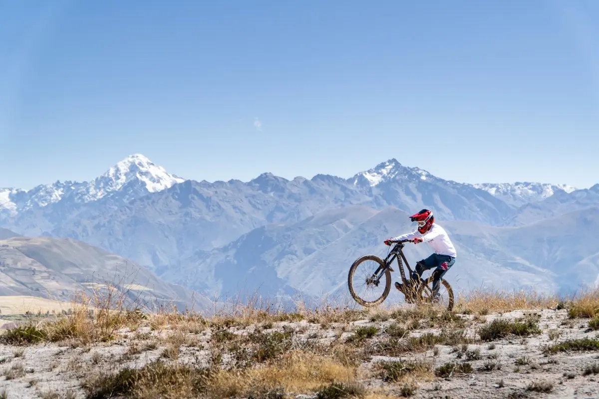 Cyclist crossing the high Maras plateau with views of the Vilcanota mountain range, among Andean grasslands and clear skies (Peru Biking Tours).