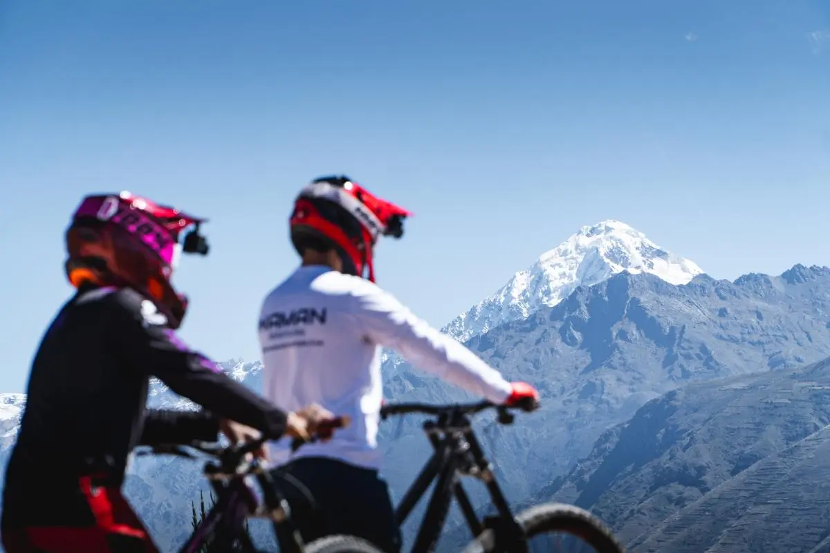 Two cyclists equipped with helmet and protection at the start of the Maras–Moray enduro descent, with snow-capped mountains and the Sacred Valley in the background (Peru Biking Tours).