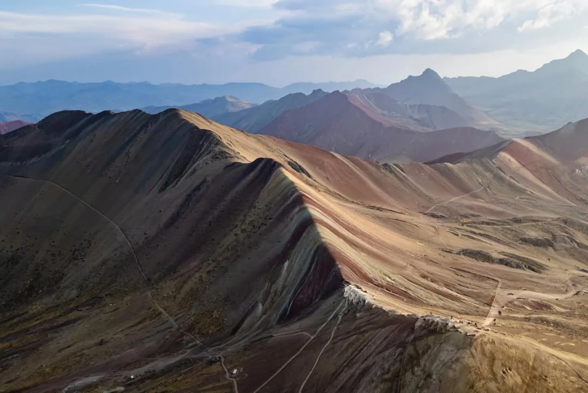 Panoramic view of Rainbow Mountain (Vinicunca) in Cusco, Peru, showing striped multicolored ridges and winding trails under a bright sky