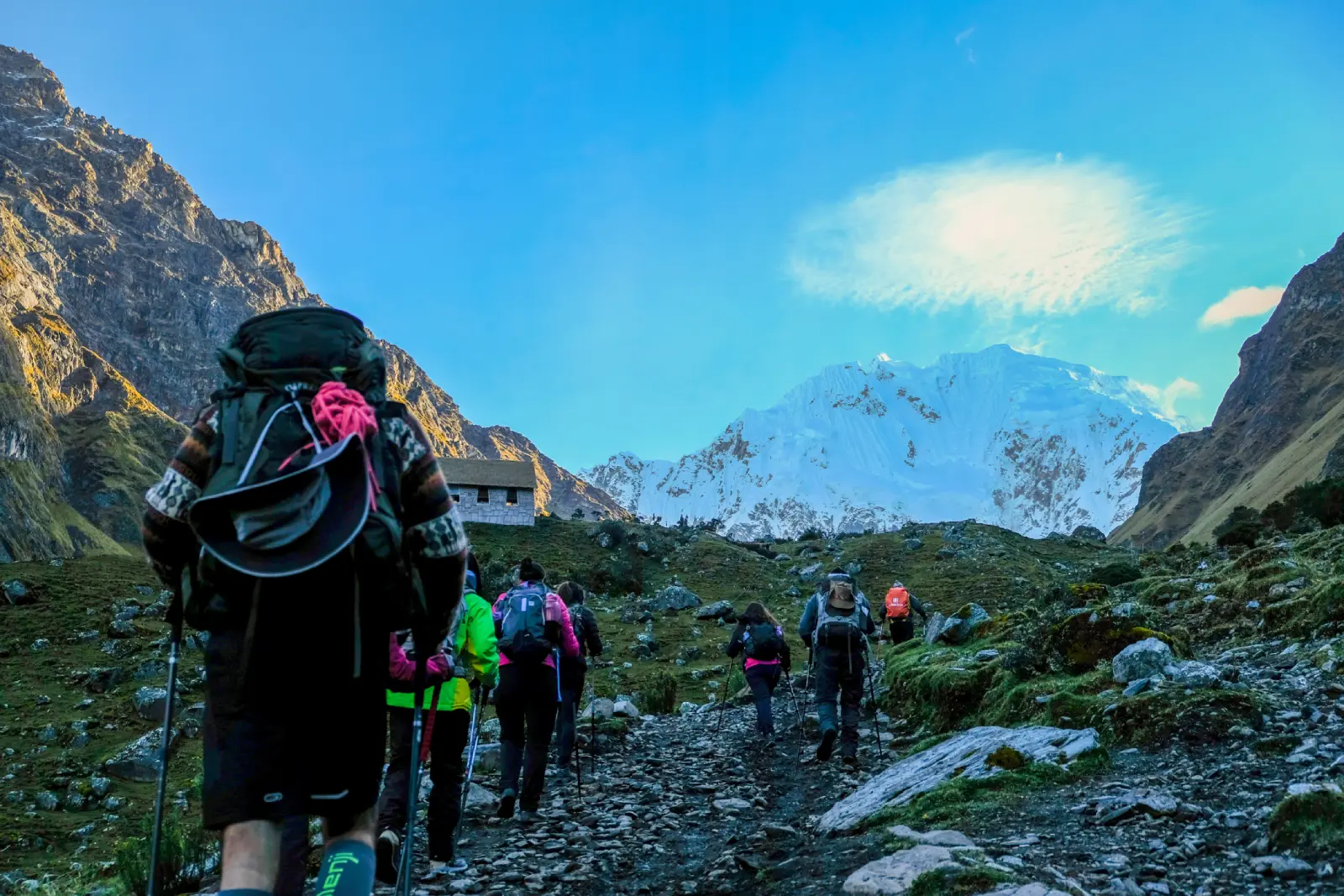 Group of trekkers walking uphill on a rocky high-Andean trail toward snow-covered Salkantay Mountain during the Salkantay Trek in Peru.