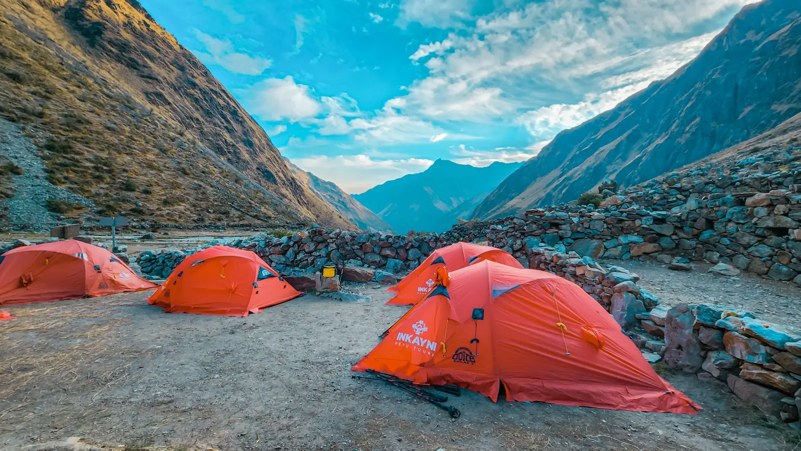 Orange trekking tents at a mountain campsite on the Salkantay Trek, surrounded by high Andean valley scenery.