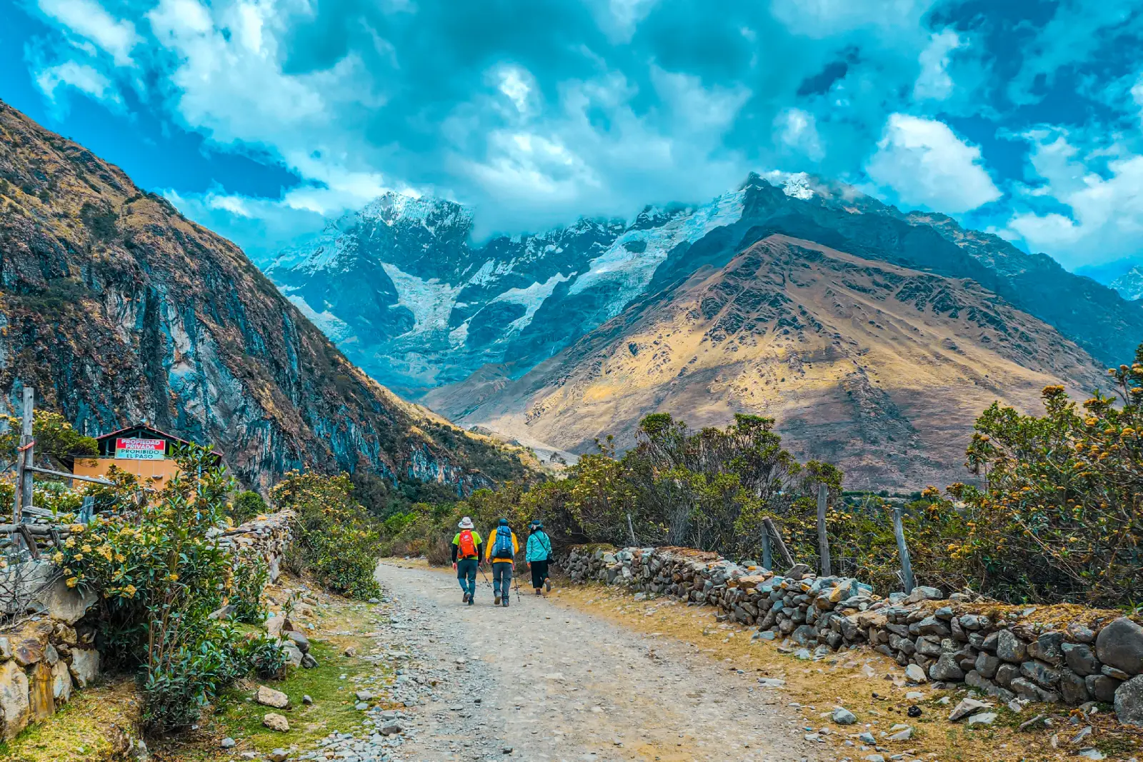 Hikers walking along the Salkantay Trek trail toward glacier-covered mountains in the high Andes.