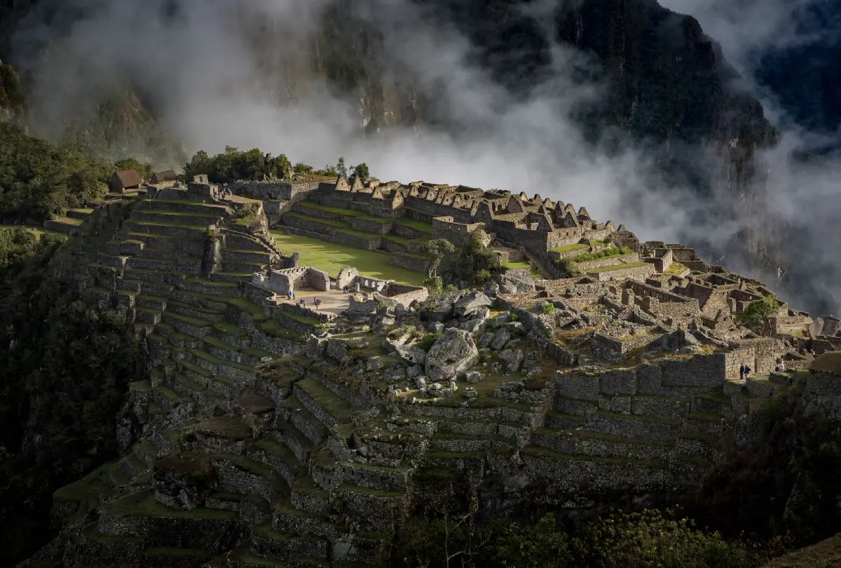 Misty morning scene at Machu Picchu showing ancient stone structures and terraced slopes at sunrise