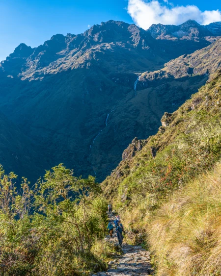 Inca Trail path with trekkers and views of an Andean valley and mountains.