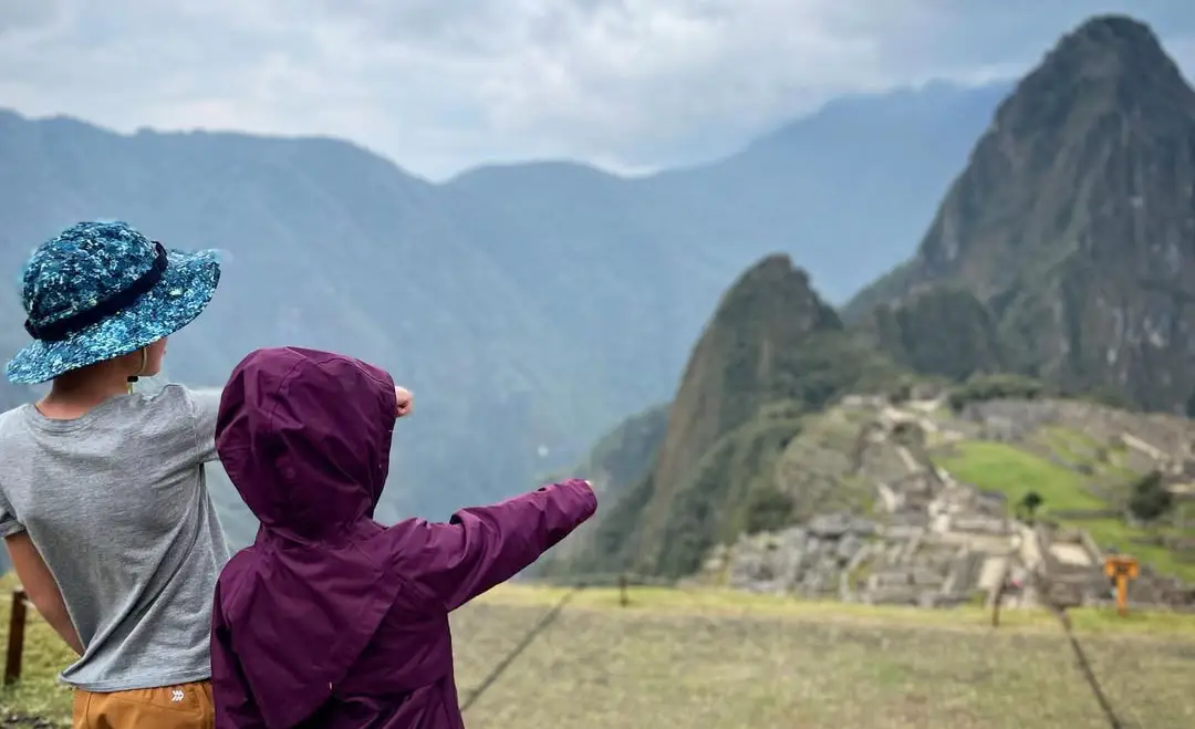 Two children pointing toward the Machu Picchu citadel from a viewpoint