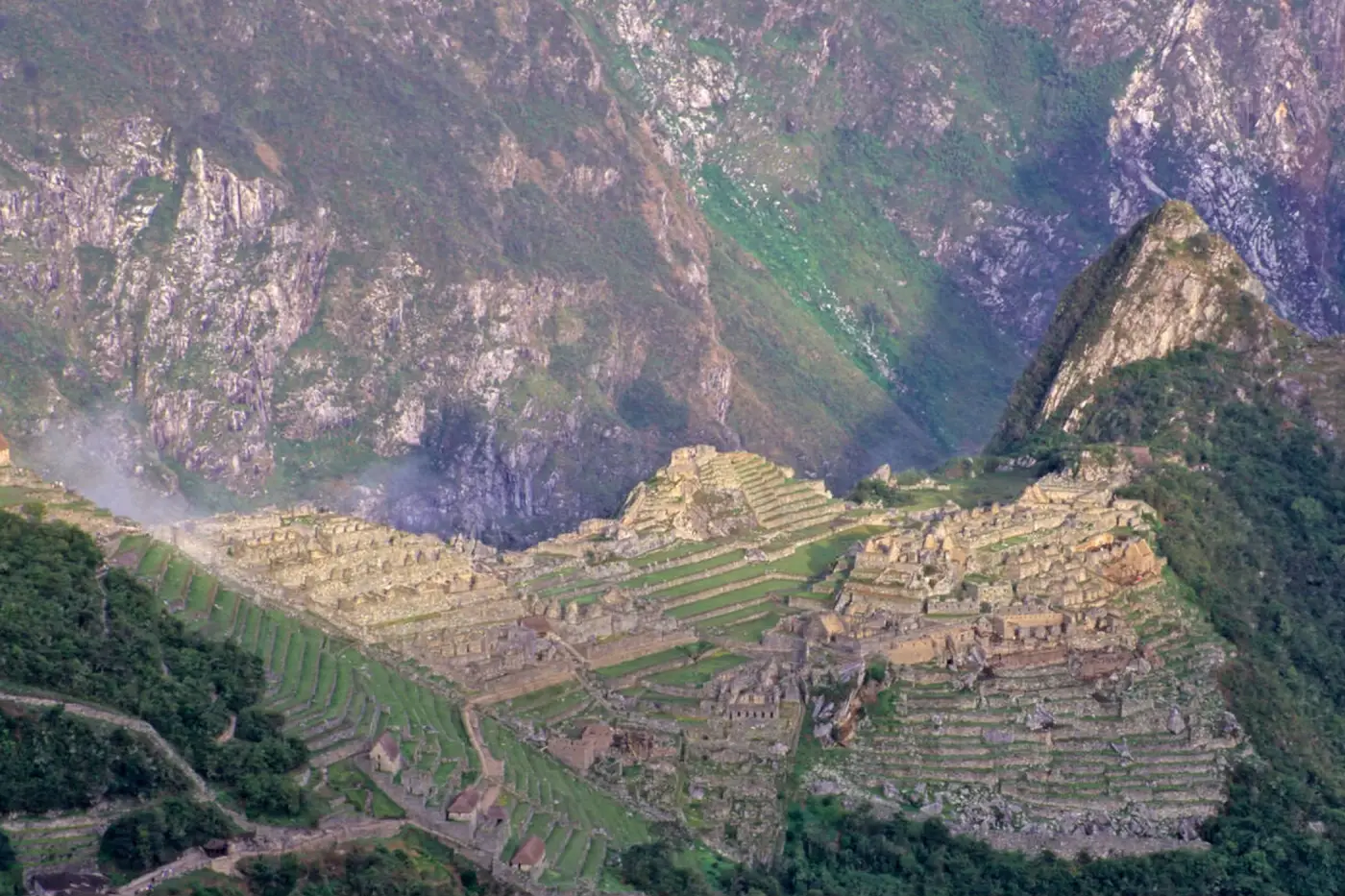 Vista panorámica de Machu Picchu desde el Intipunku, mostrando las terrazas incas, la ciudadela arqueológica, el Huayna Picchu y las montañas verdes del Santuario Histórico.