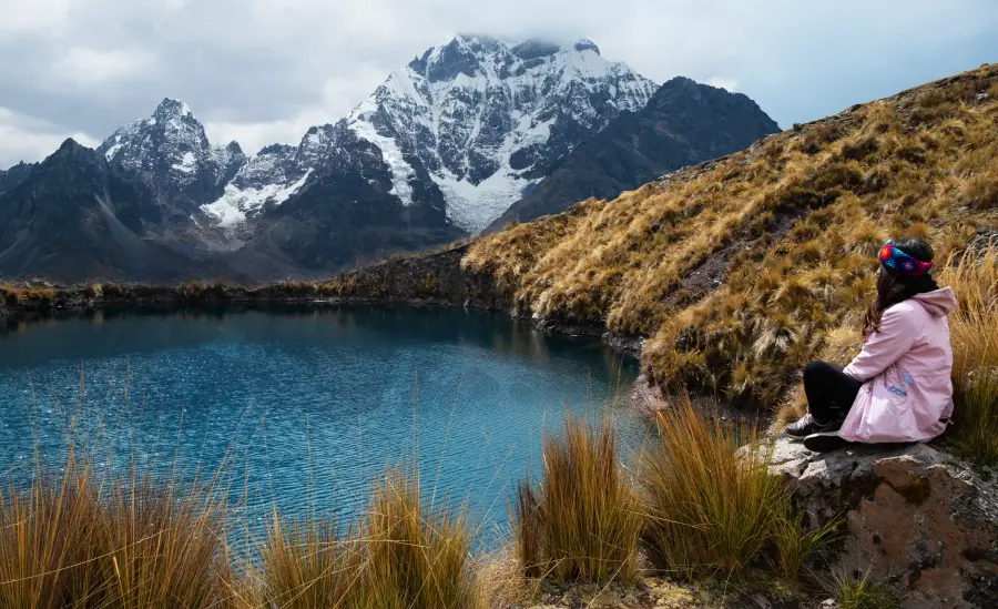 Mujer sentada en una roca frente a una de las 7 lagunas de Ausangate.