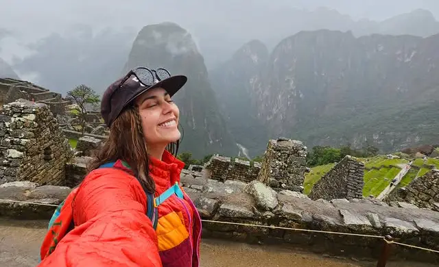 Mujer sonriendo bajo la lluvia en Machu Picchu.