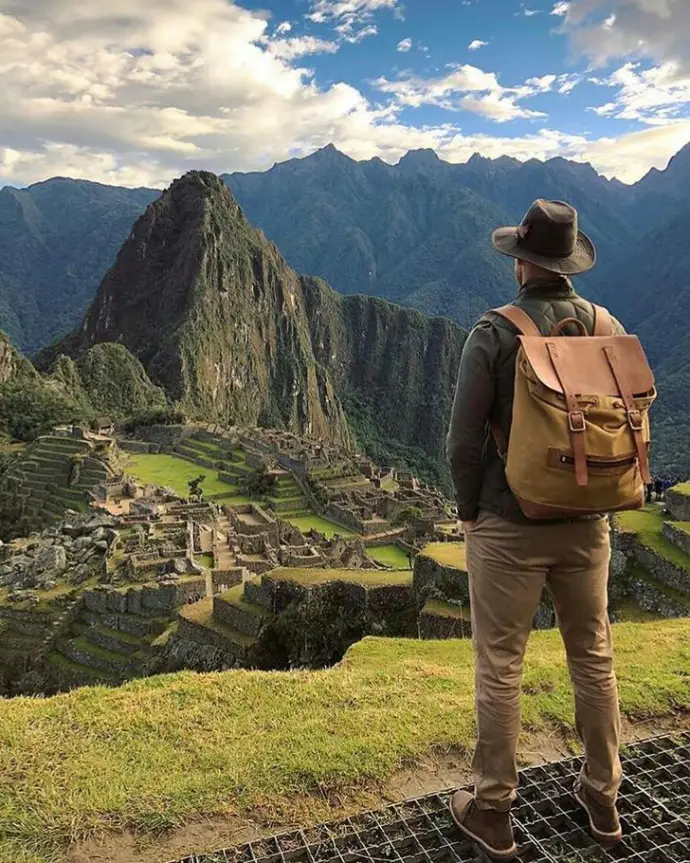 Traveler with backpack and hat looking toward Machu Picchu mountains during sunrise