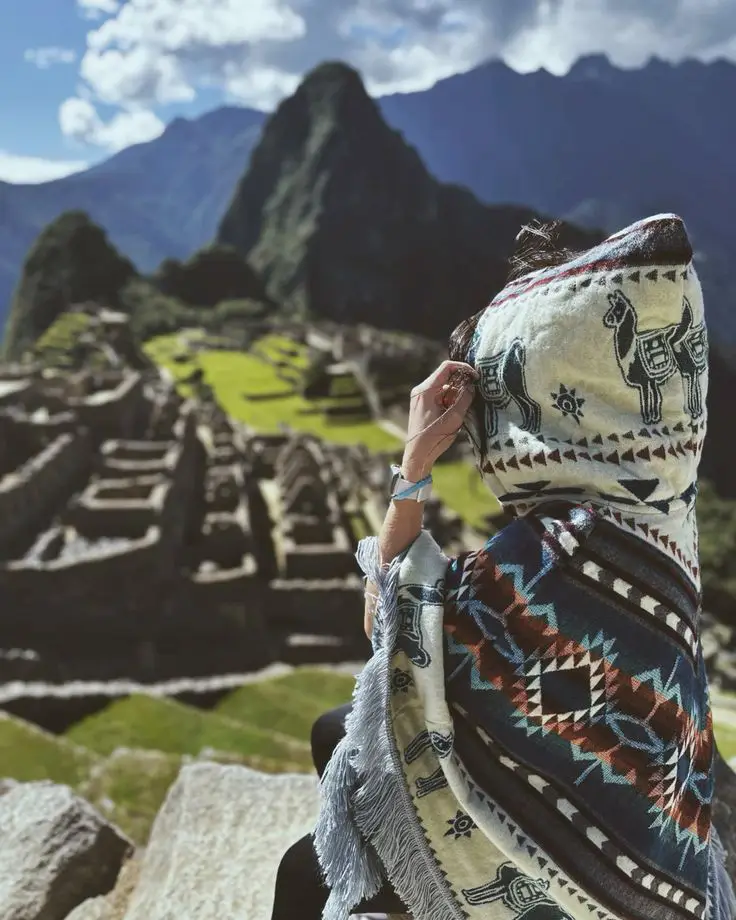 Traveler watching the sunrise at Machu Picchu with mountain light, clouds, and vegetation