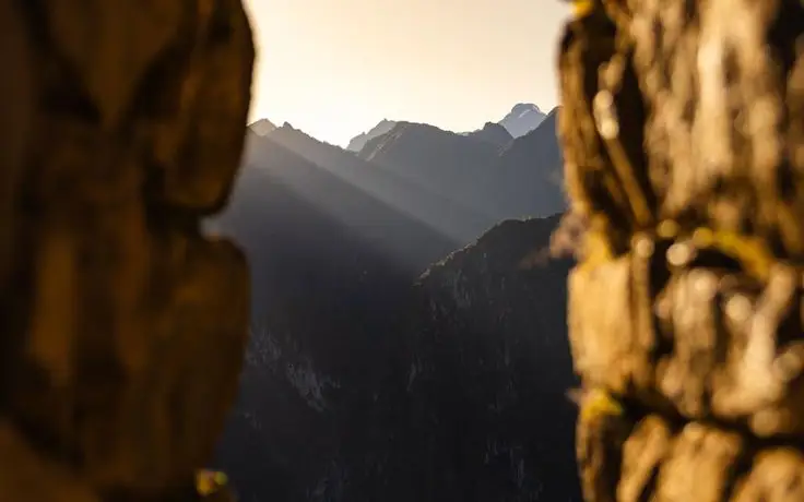 Sunrise rays passing through a stone opening at Machu Picchu with yellow morning sky and mountains