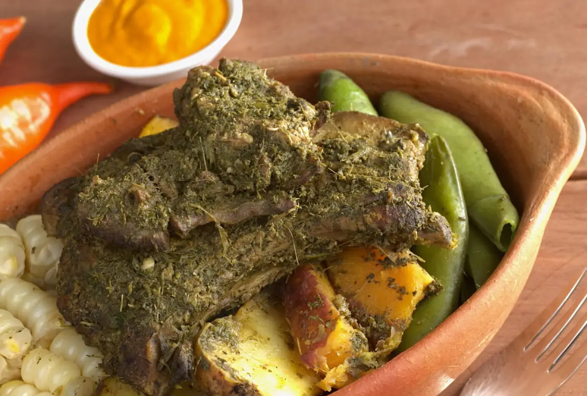Traditional pachamanca served in a clay dish with seasoned meats, Andean tubers, corn, fava beans and chili sauce.