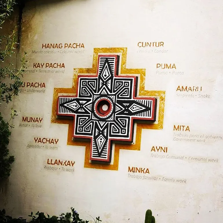 Wall mural of an Andean chakana cross with Spanish labels explaining Hanan Pacha, Kay Pacha, Ukhu Pacha, and symbols like condor, puma, and snake.