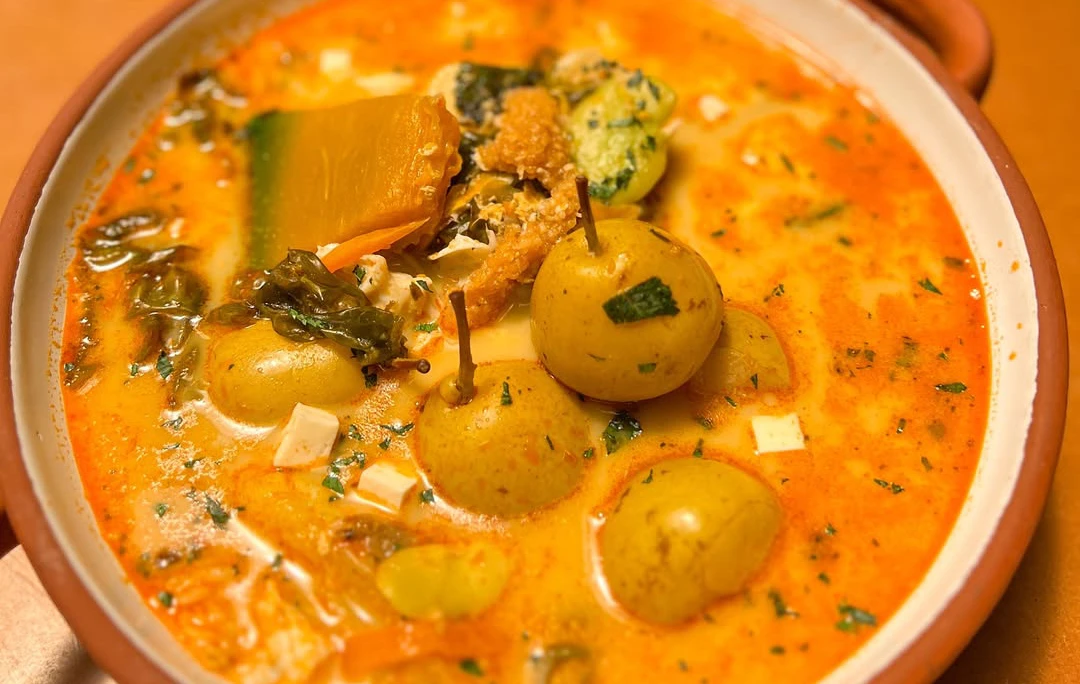 Bowl of Cusco-style chupe de pera with pears, cheese, vegetables, and herbs in a creamy orange Andean broth