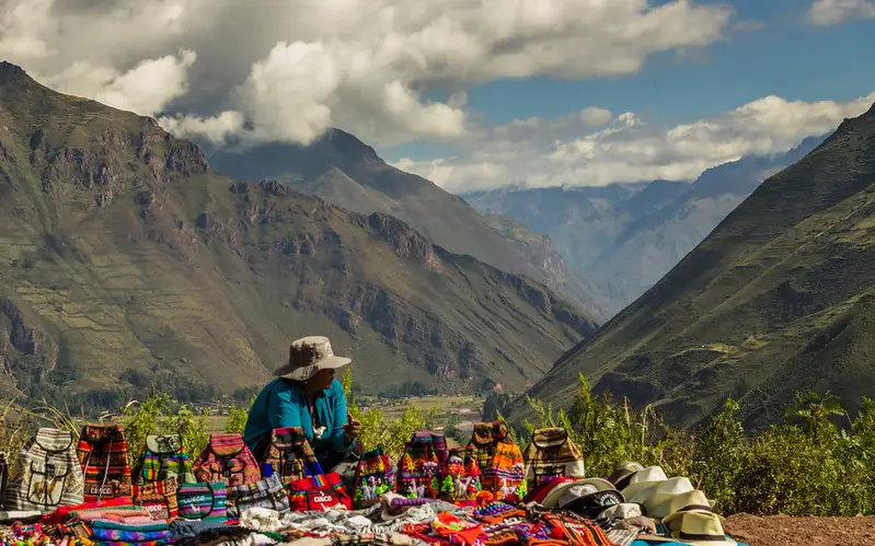 Vendedora de artesanías en una carretera de Cusco con montañas y nubes de fondo.