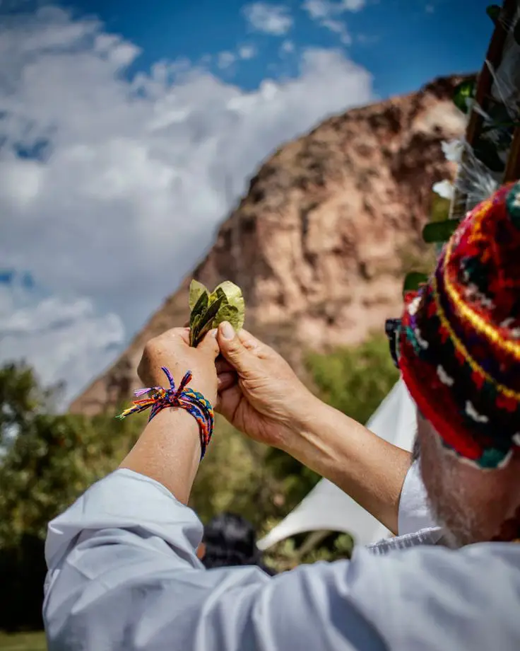 Hombre realizando ofrenda de hojas de coca en honor a la Pachamama (Madre Tierra).
