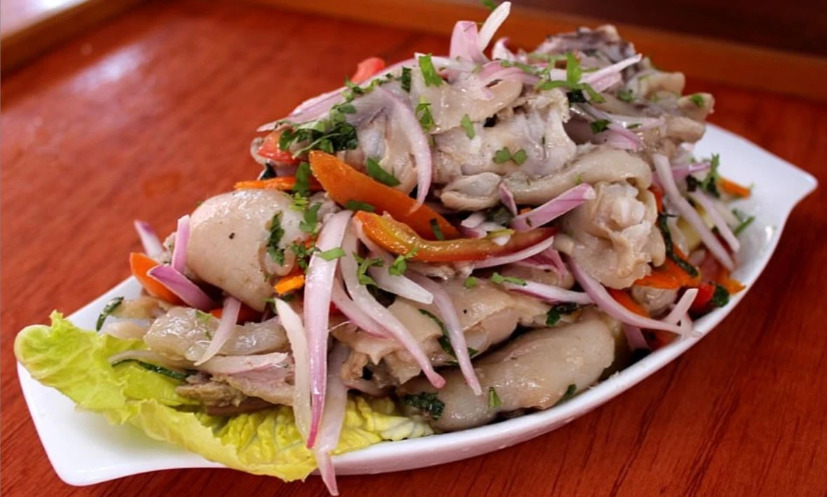 Plate of zarza de patitas, a Cusco-style pig’s feet salad with sliced red onion, herbs, and vegetables served on lettuce.