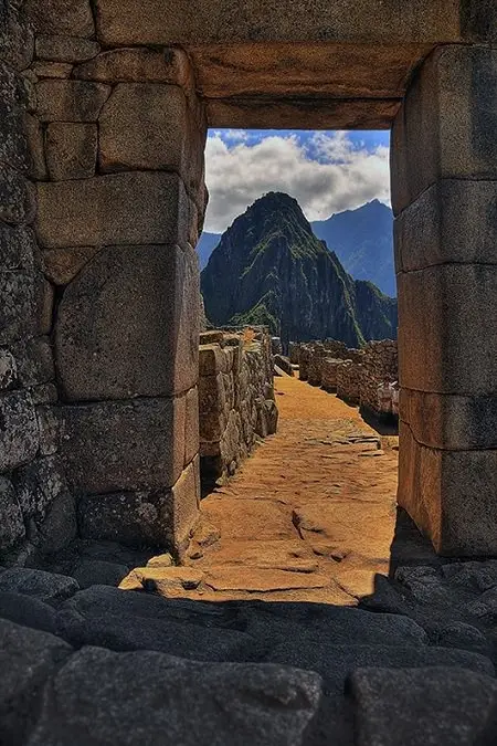 Sendero de piedra de Machu Picchu y montañas bajo el sol y las nubes de la mañana