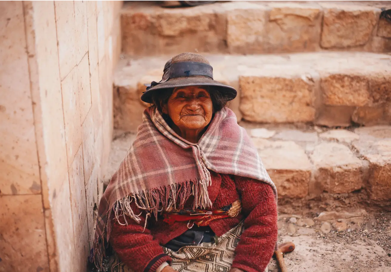dulce sentada abrigada sonrisa ojos pequeños algunas arrugas piel trigueña compasiva
