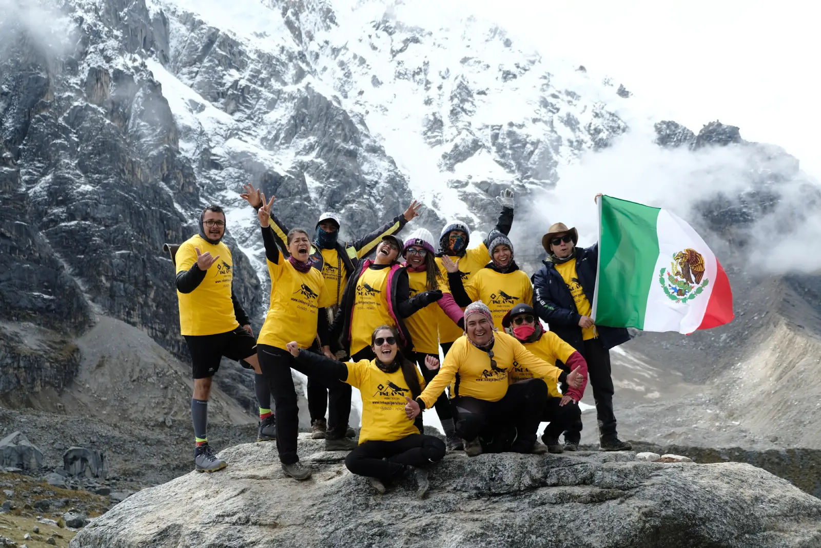 Group of trekkers posing with a Mexican flag in front of Salkantay mountain’s snowy face.