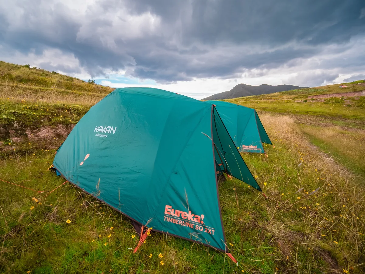 Tienda de camping Eureka instalada en terreno andino con césped bajo un cielo nublado.
